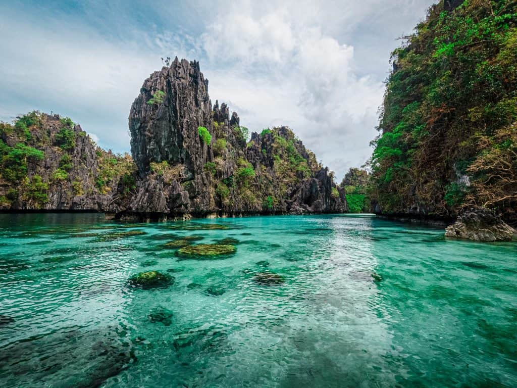 Crystal-clear turquoise waters of Big Lagoon in El Nido, Palawan, Philippines, surrounded by towering limestone cliffs and lush greenery, a top tropical travel destination.