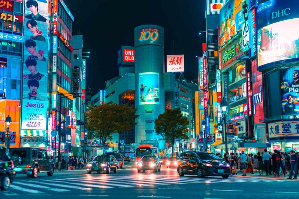 Vibrant nighttime scene at Shibuya Crossing in Tokyo, Japan, featuring neon-lit billboards, busy traffic, and crowds of pedestrians, capturing the city's dynamic urban energy.